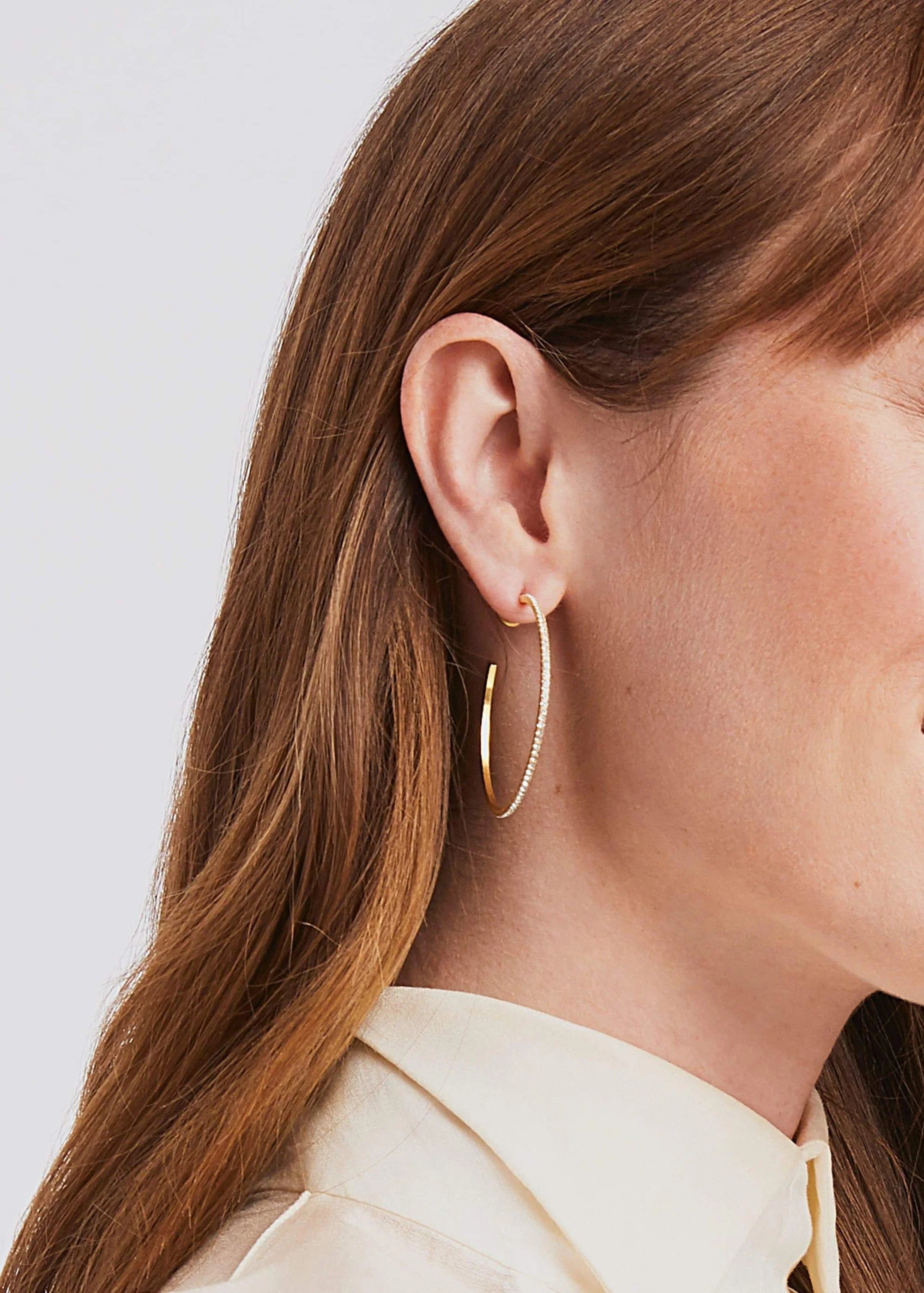Close-up of a woman wearing gold hoop earrings with a plain background