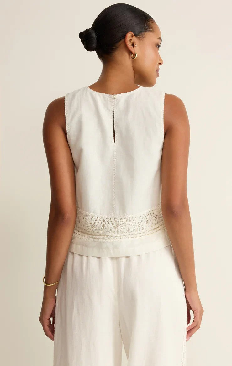 Woman wearing a white sleeveless top with lace details on a beige background