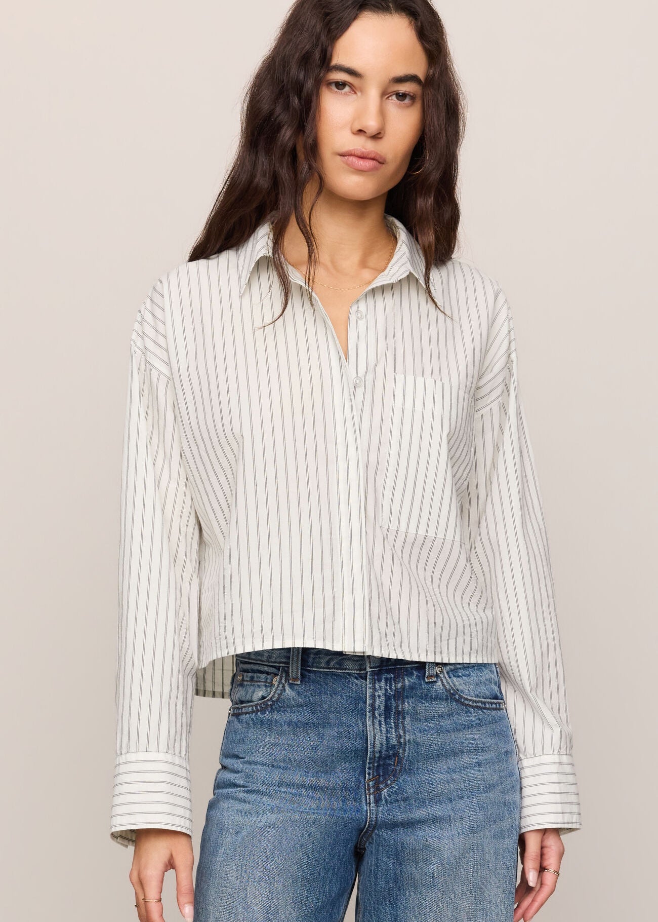 Woman wearing a striped shirt and blue jeans against a plain background