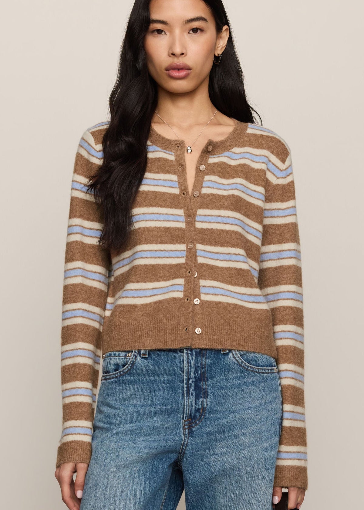 Woman wearing a brown striped sweater and blue jeans against a beige background