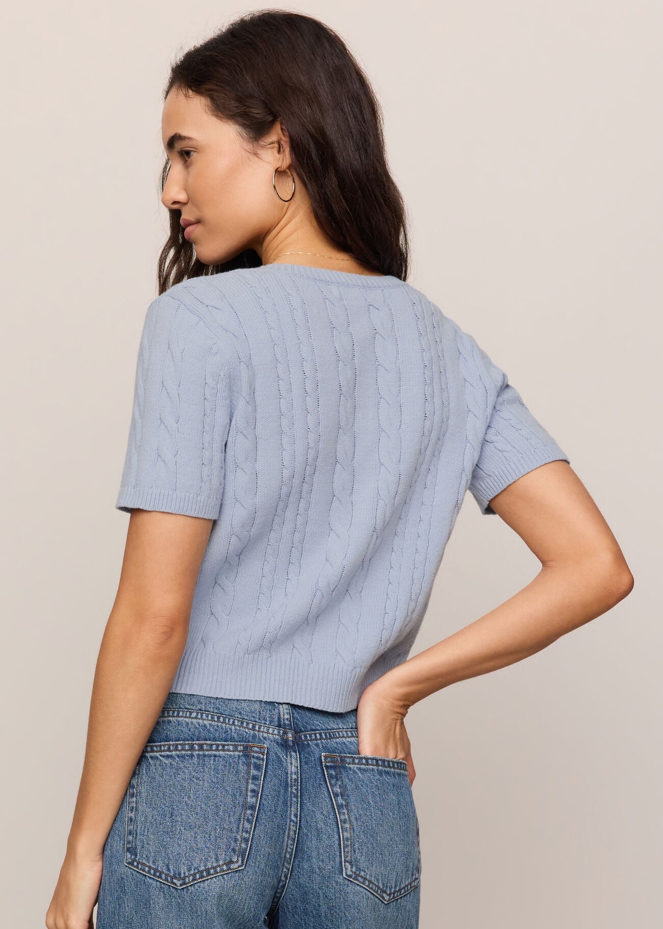 Woman wearing a light blue textured top and jeans on a beige background