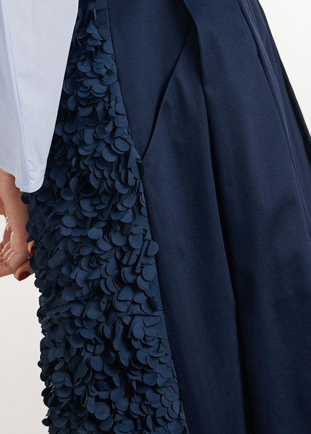 Close-up of a navy blue garment with a heavily textured, layered scalloped fabric panel and a hand adjusting a white sleeve.