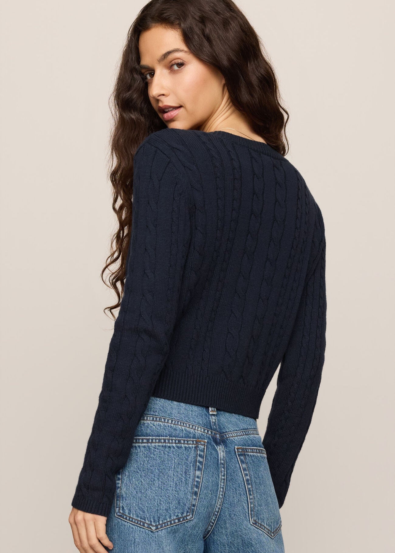 Woman wearing a navy sweater and blue jeans on a beige background