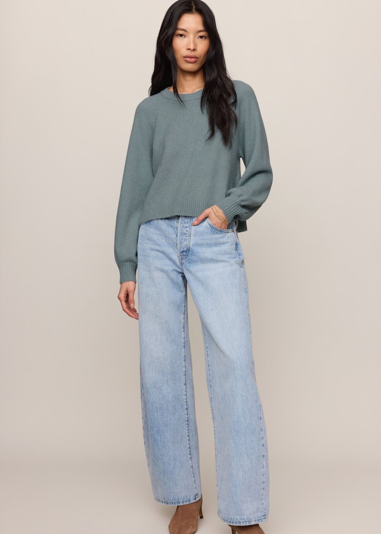 Woman wearing a green sweater and light blue jeans on a beige background