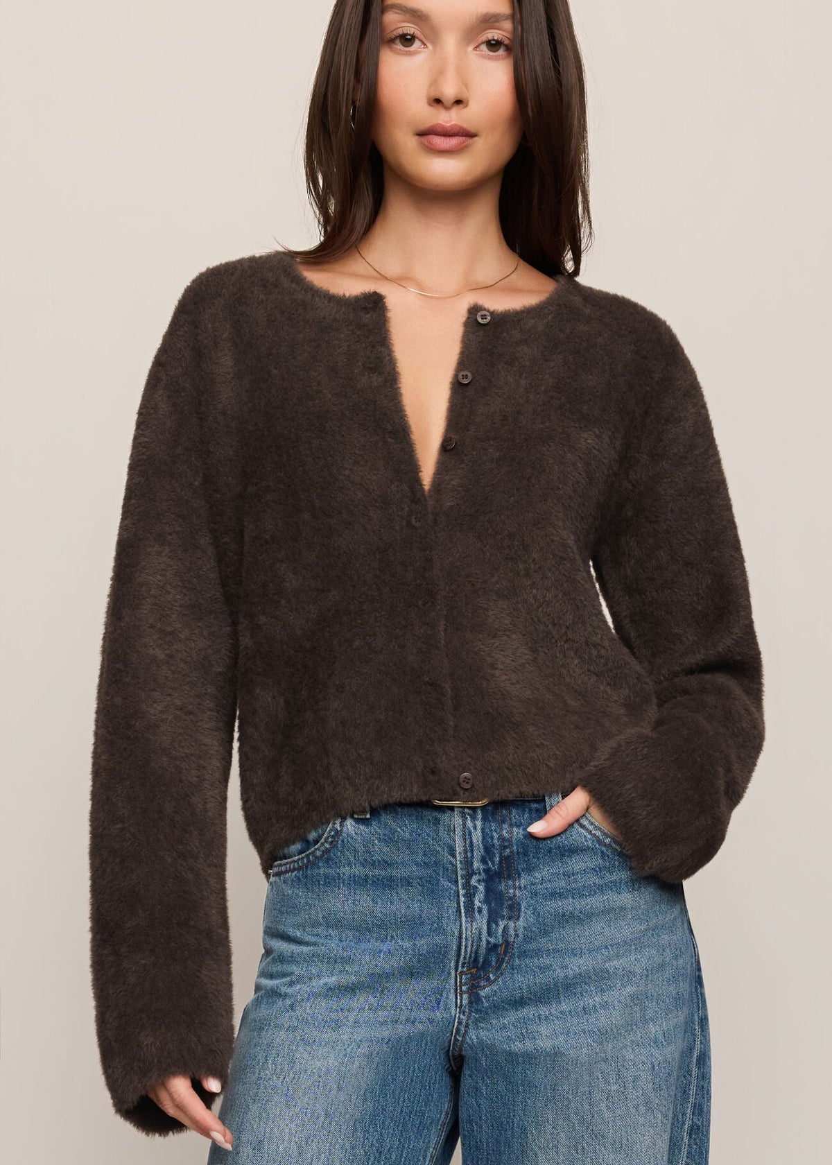 Woman wearing a dark brown sweater and blue jeans against a plain background