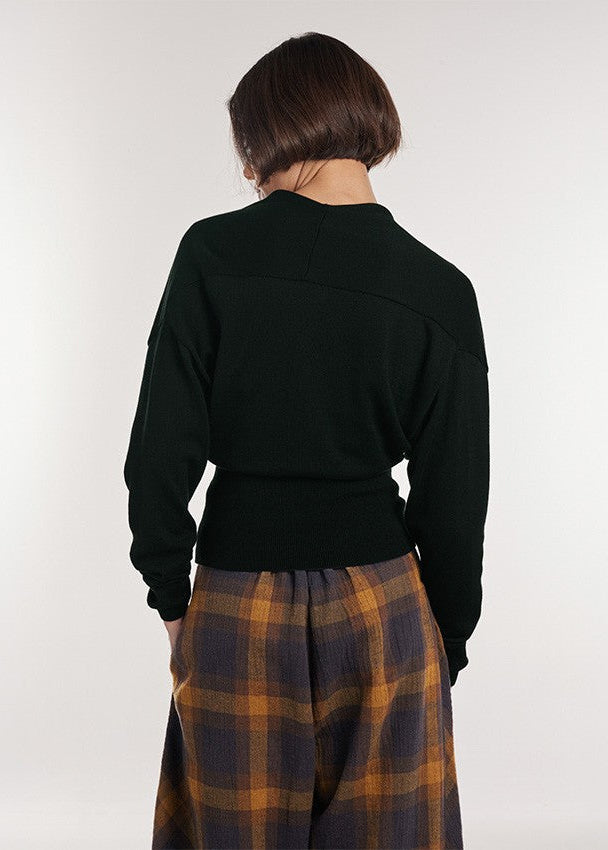 A model shown from the back wearing a dark green long-sleeve crop top and a brown and orange plaid skirt, against a plain light gray background.