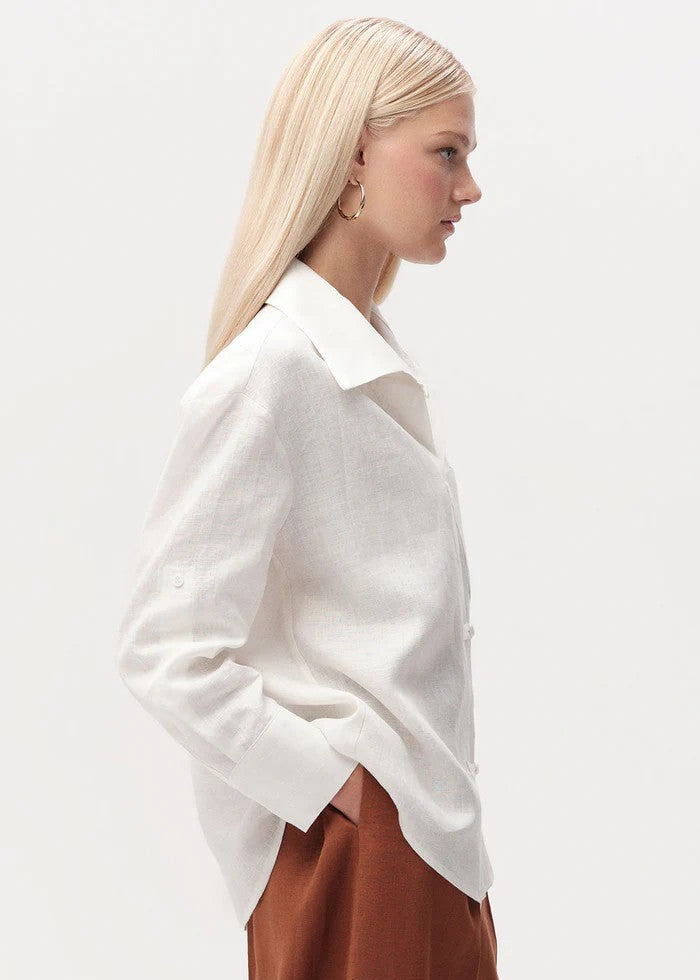 Person wearing a white oversized shirt and brown pants on a light gray background