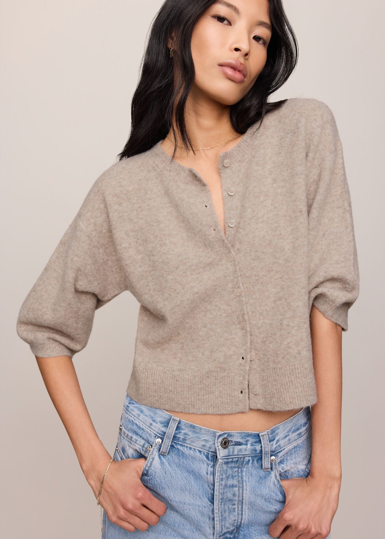 Woman wearing a beige button-up shirt and blue jeans against a plain background