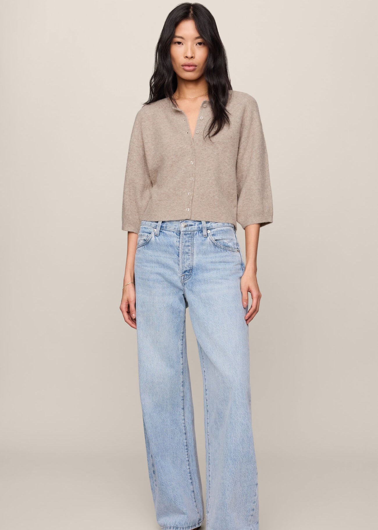 Woman wearing a beige shirt and light blue jeans against a plain background