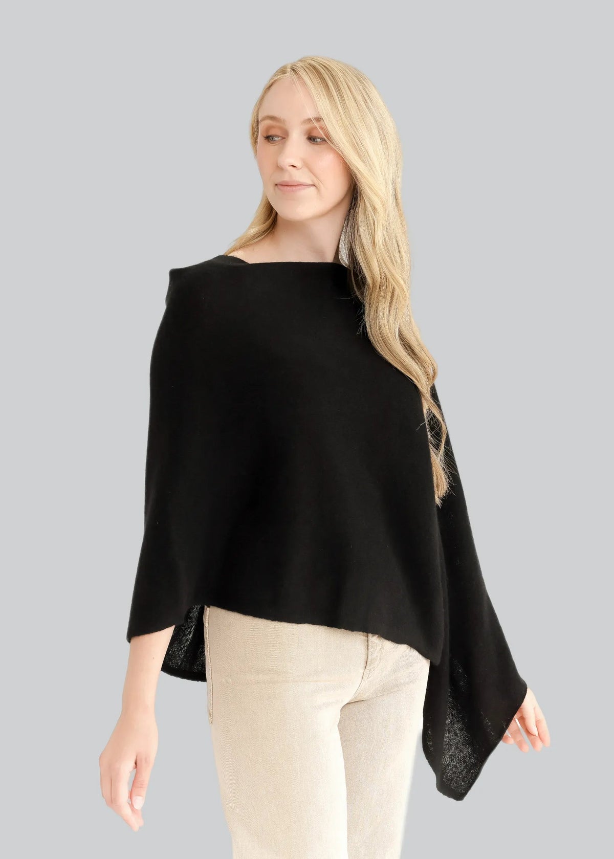 Woman wearing a black poncho over a beige top and pants on a white background