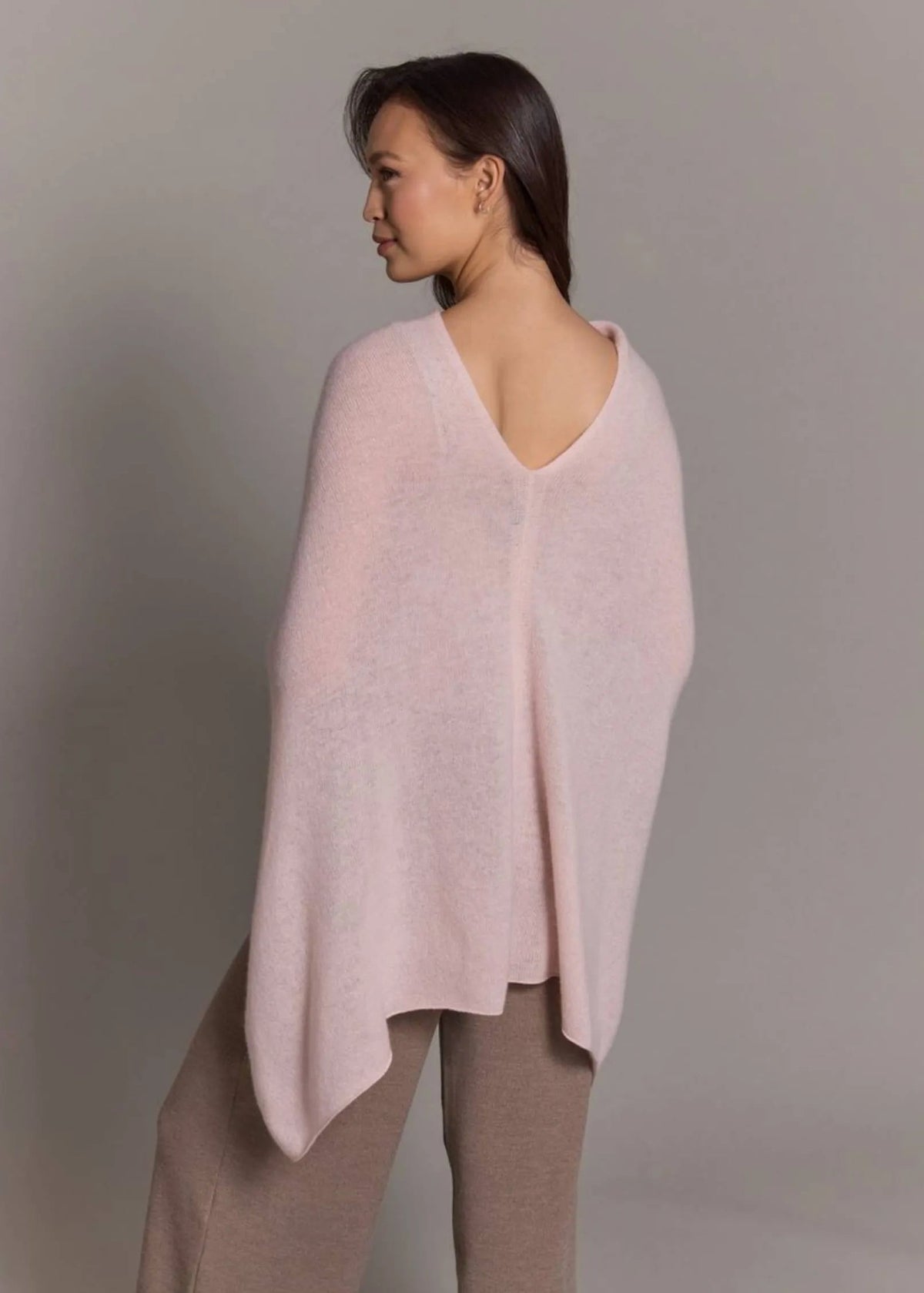Woman wearing a light pink poncho against a plain background