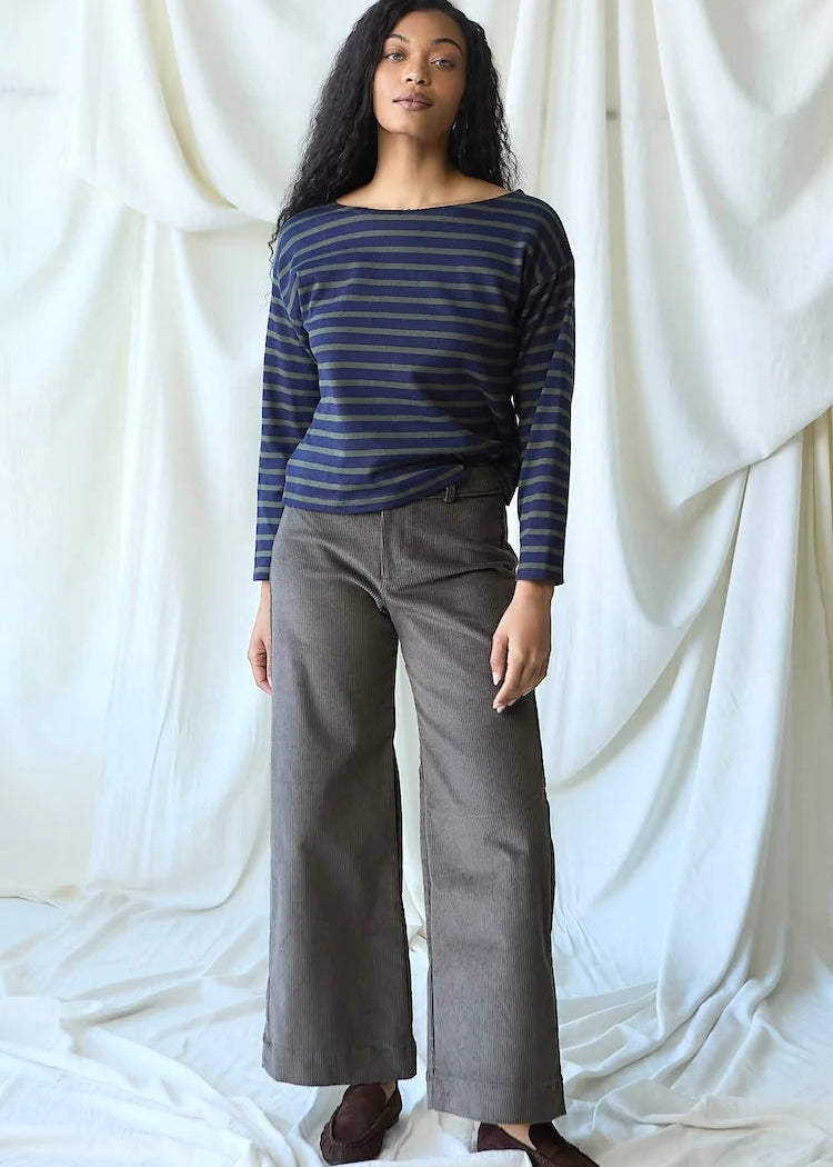 A woman modeling a navy blue and gray striped long-sleeve top with wide-leg gray trousers, standing against a draped white fabric backdrop.