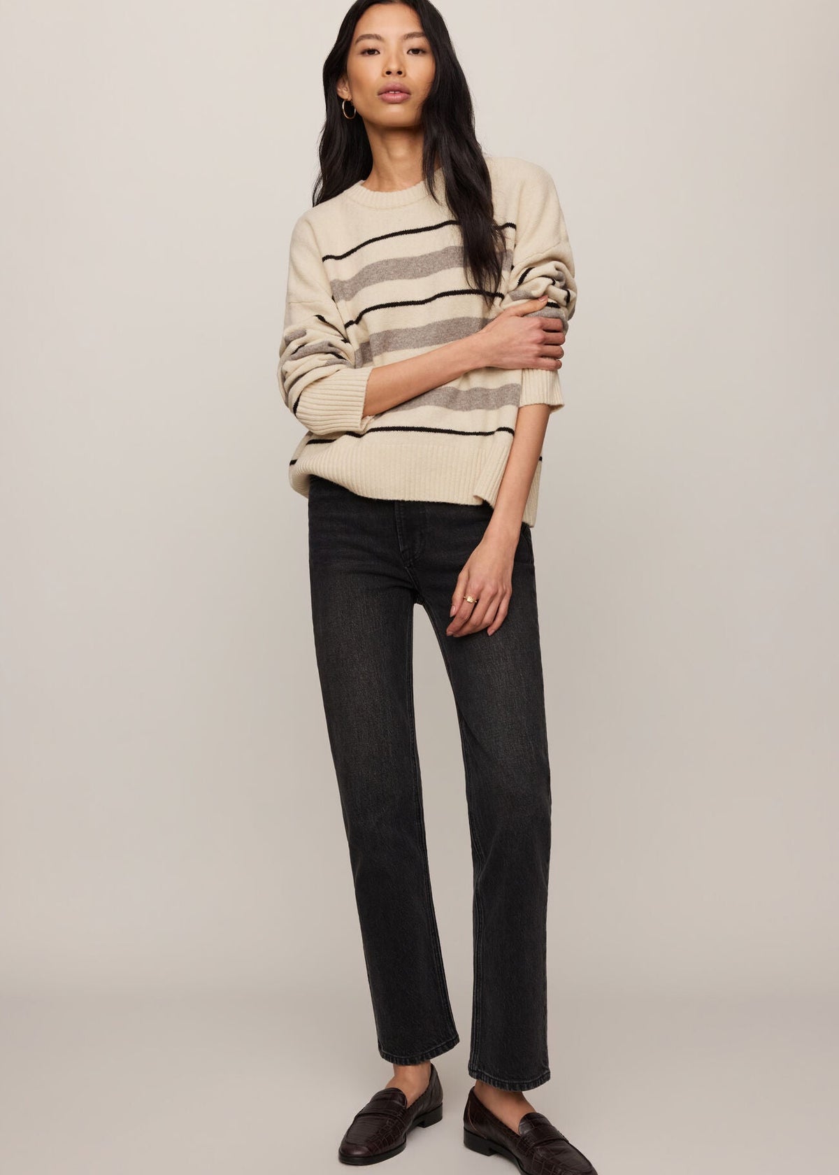 Woman wearing a striped sweater and black pants on a plain background