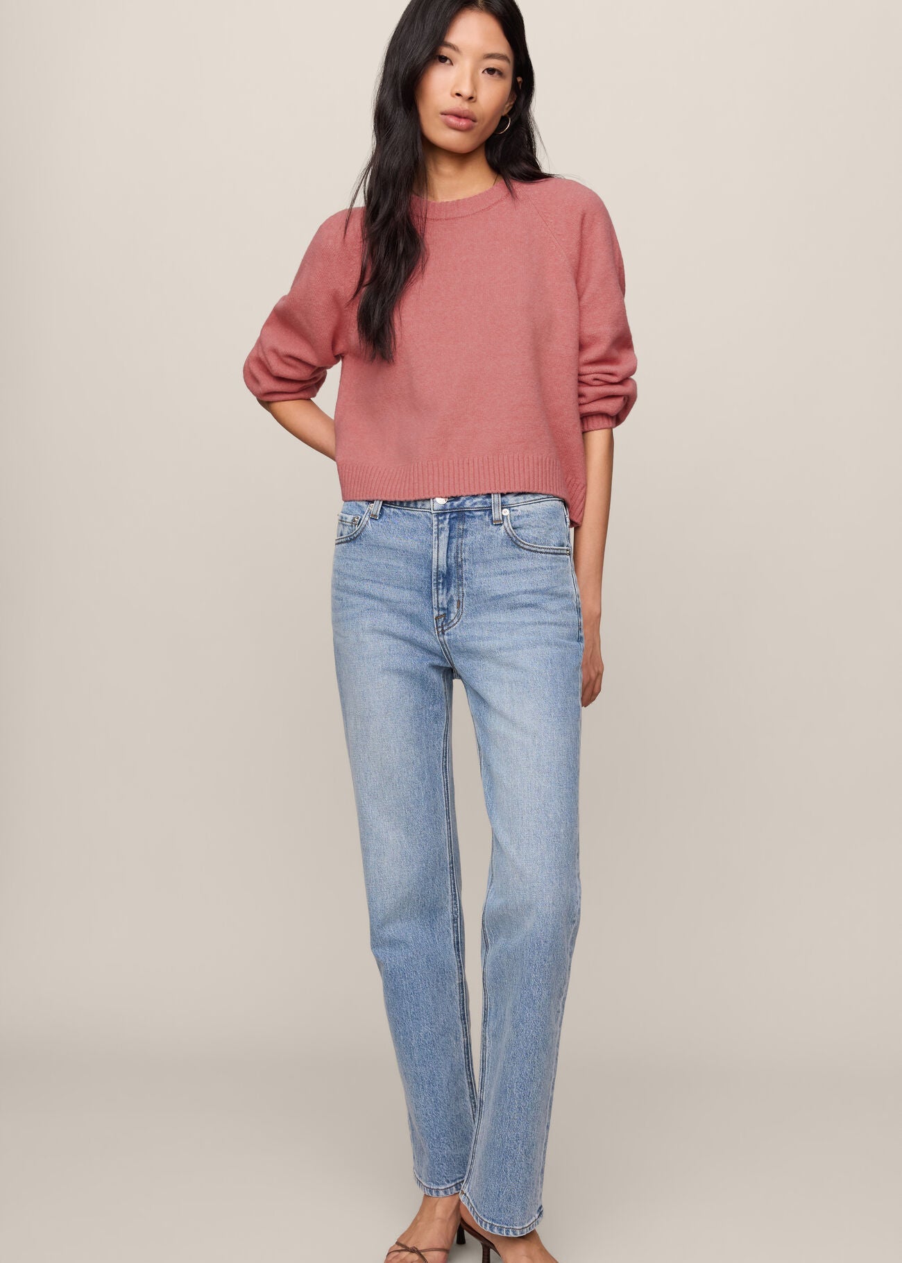 Woman wearing a pink sweater and light blue jeans on a beige background