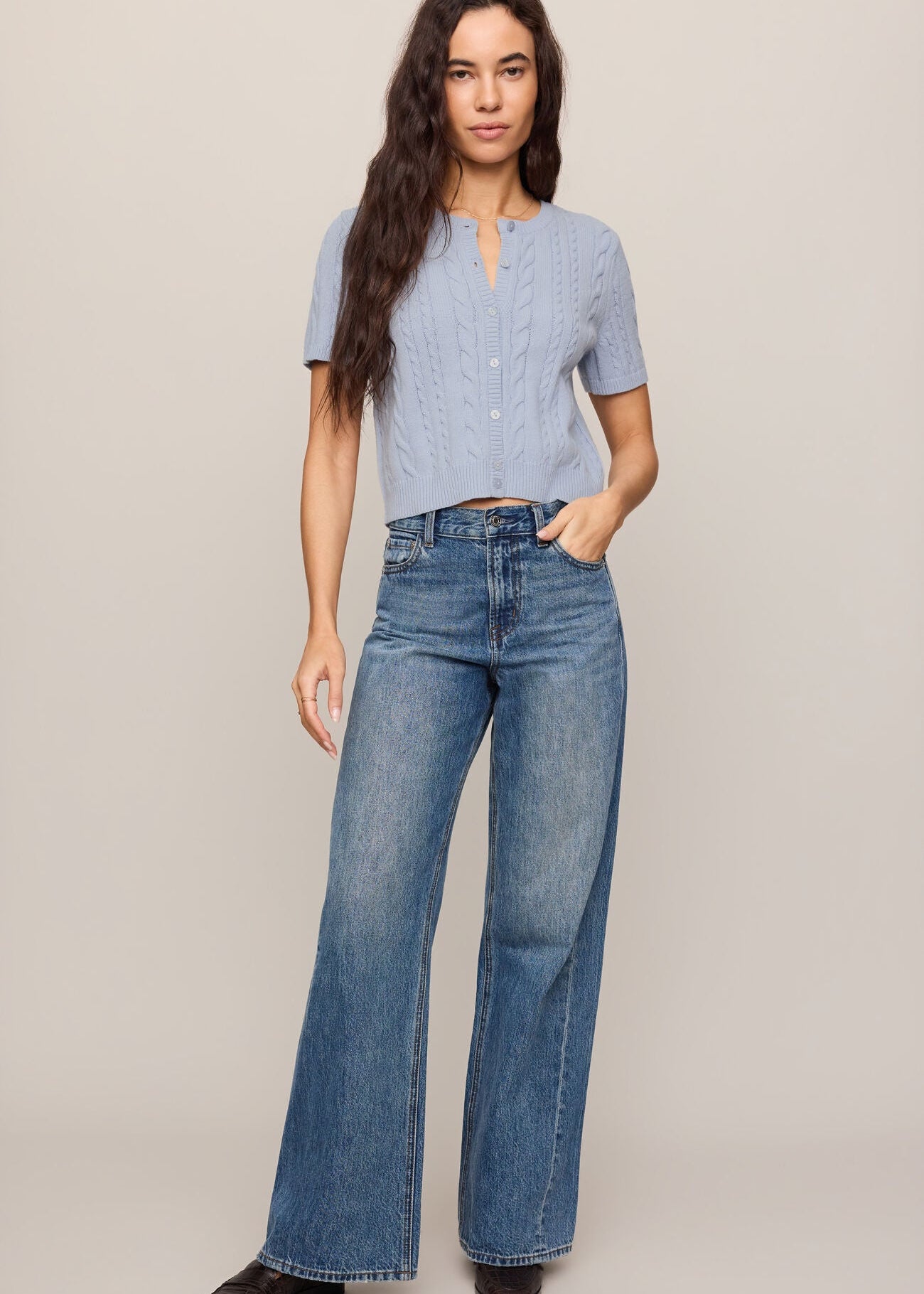 Woman wearing a light blue button-up shirt and blue jeans on a beige background