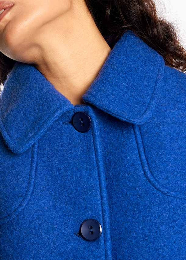 Close-up of a person wearing a bright royal blue wool-blend coat with a wide collar and dark buttons.