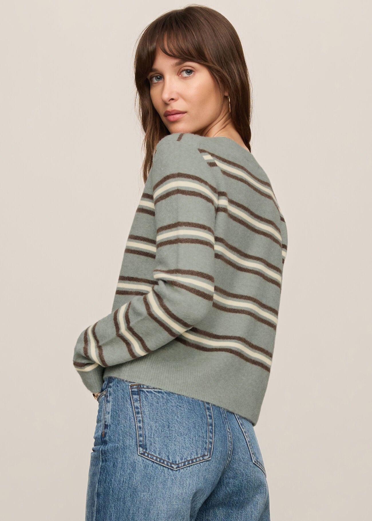 Woman wearing a striped sweater and jeans against a plain background