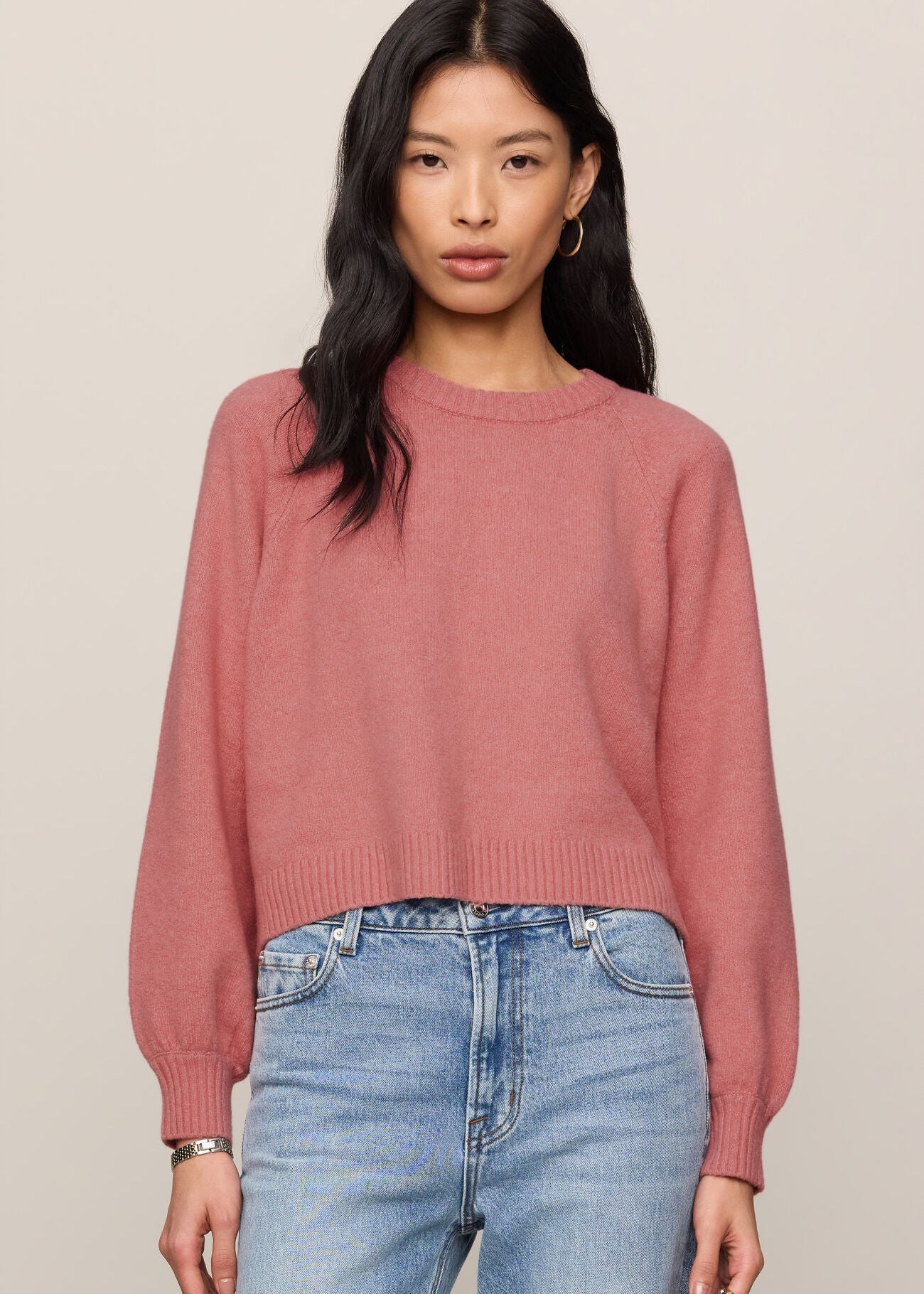 Woman wearing a pink sweater and blue jeans against a beige background