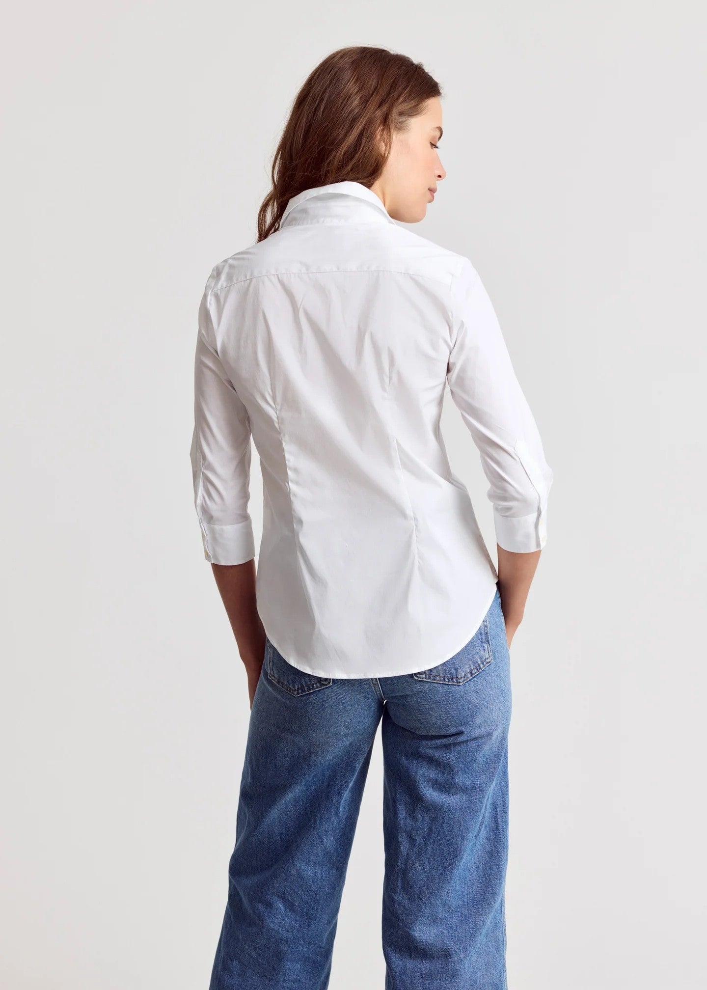 Person wearing a white shirt and blue jeans on a light gray background