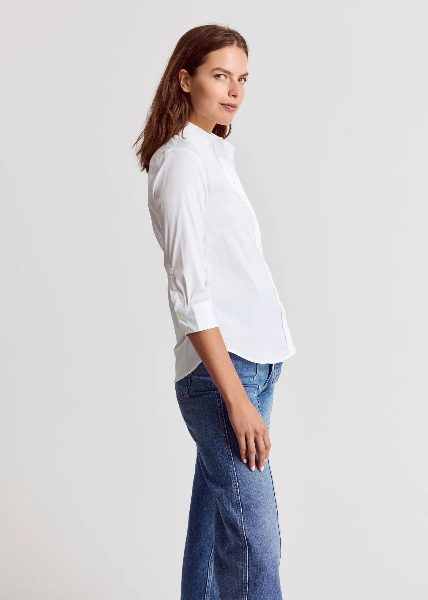 Woman wearing a white shirt and blue jeans against a plain background