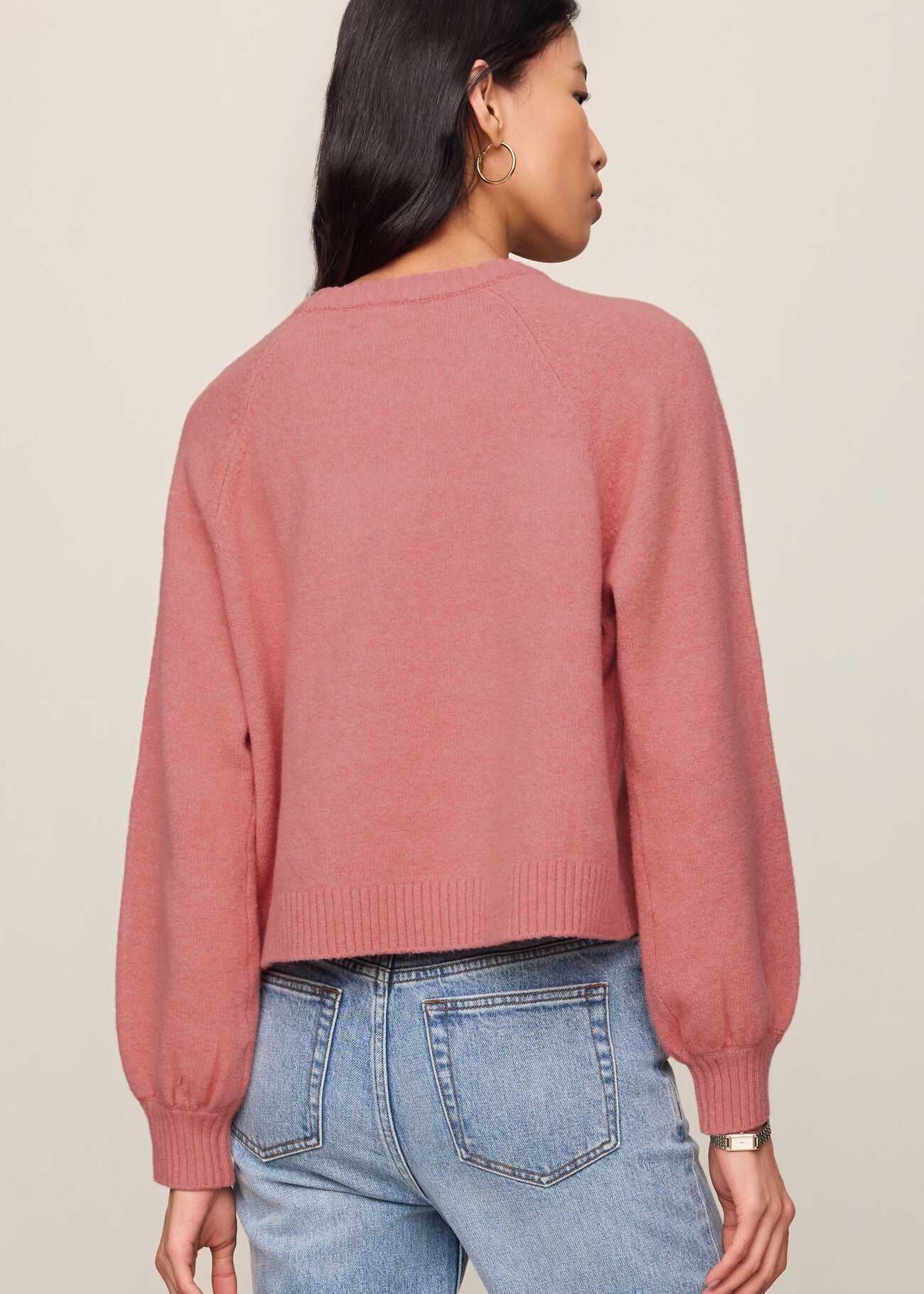 Person wearing a pink sweater and blue jeans on a plain background