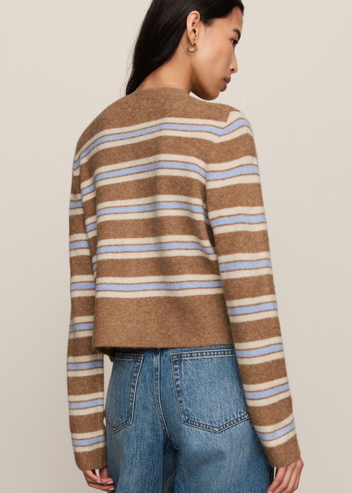 Person wearing a brown and blue striped sweater with blue jeans on a beige background