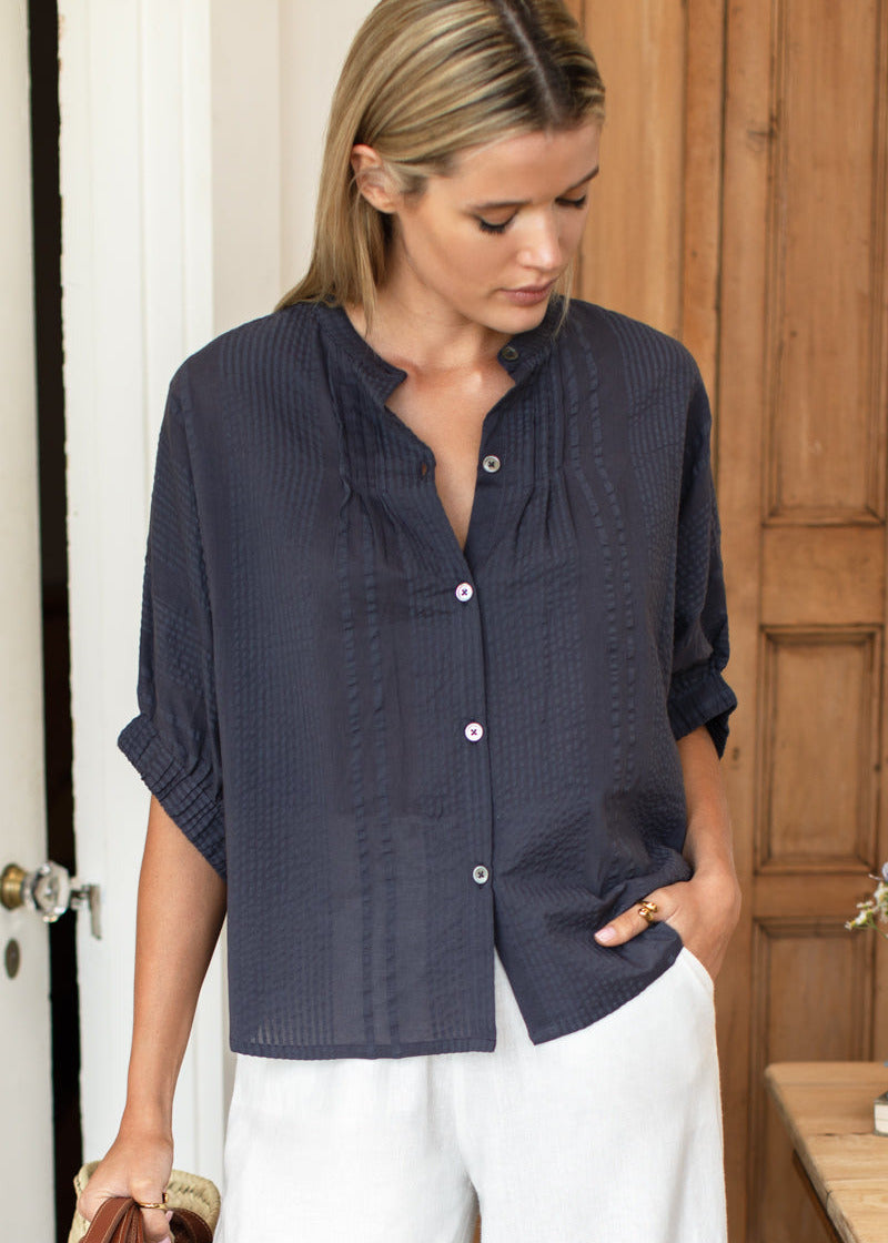 Woman wearing a navy blue textured shirt and white pants indoors.
