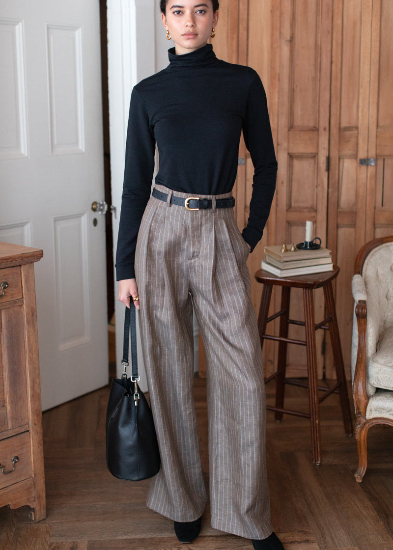 Woman in black turtleneck and gray plaid pants standing in a room with wooden furniture.