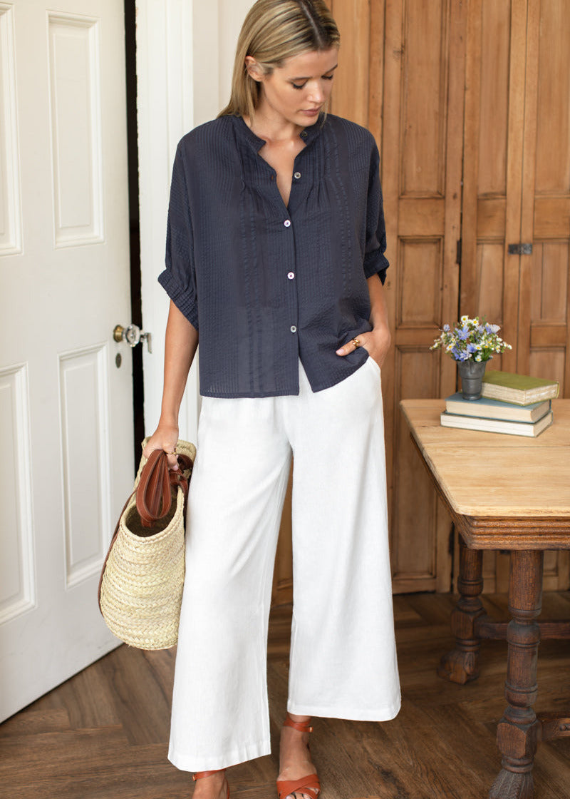 Woman in navy shirt and white pants standing in a room with wooden floor and furniture.