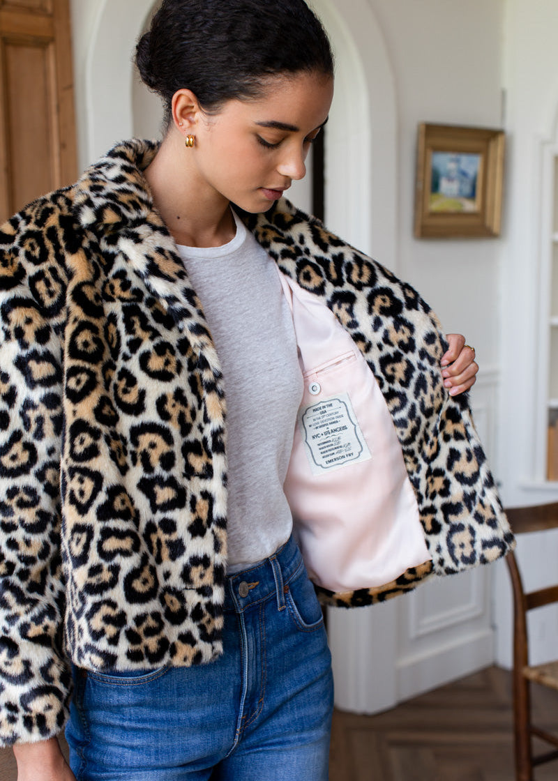 A woman wearing a plush leopard-print faux fur jacket with a light pink lining, shown in a home interior setting.