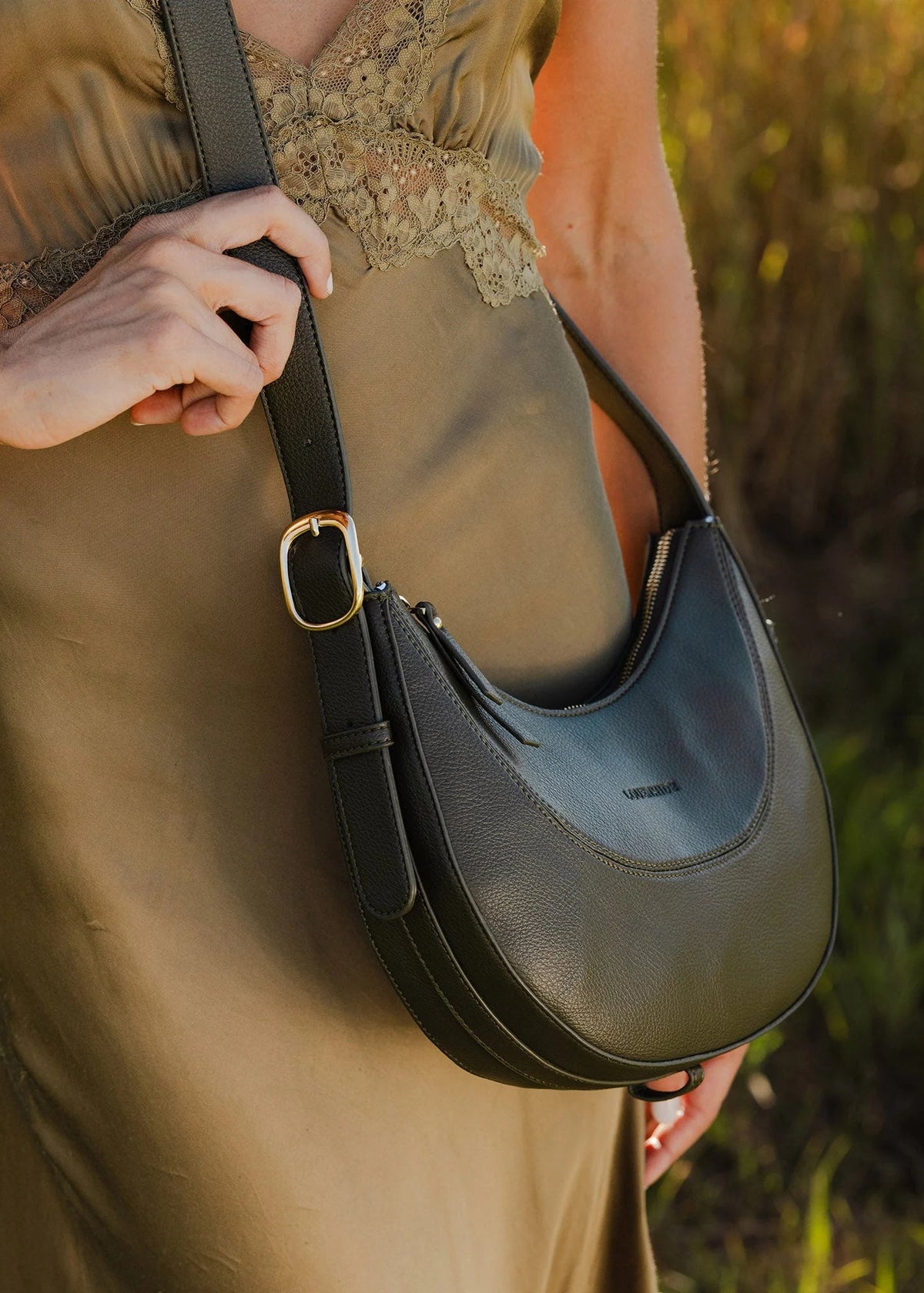 Person holding a black leather handbag in a natural setting