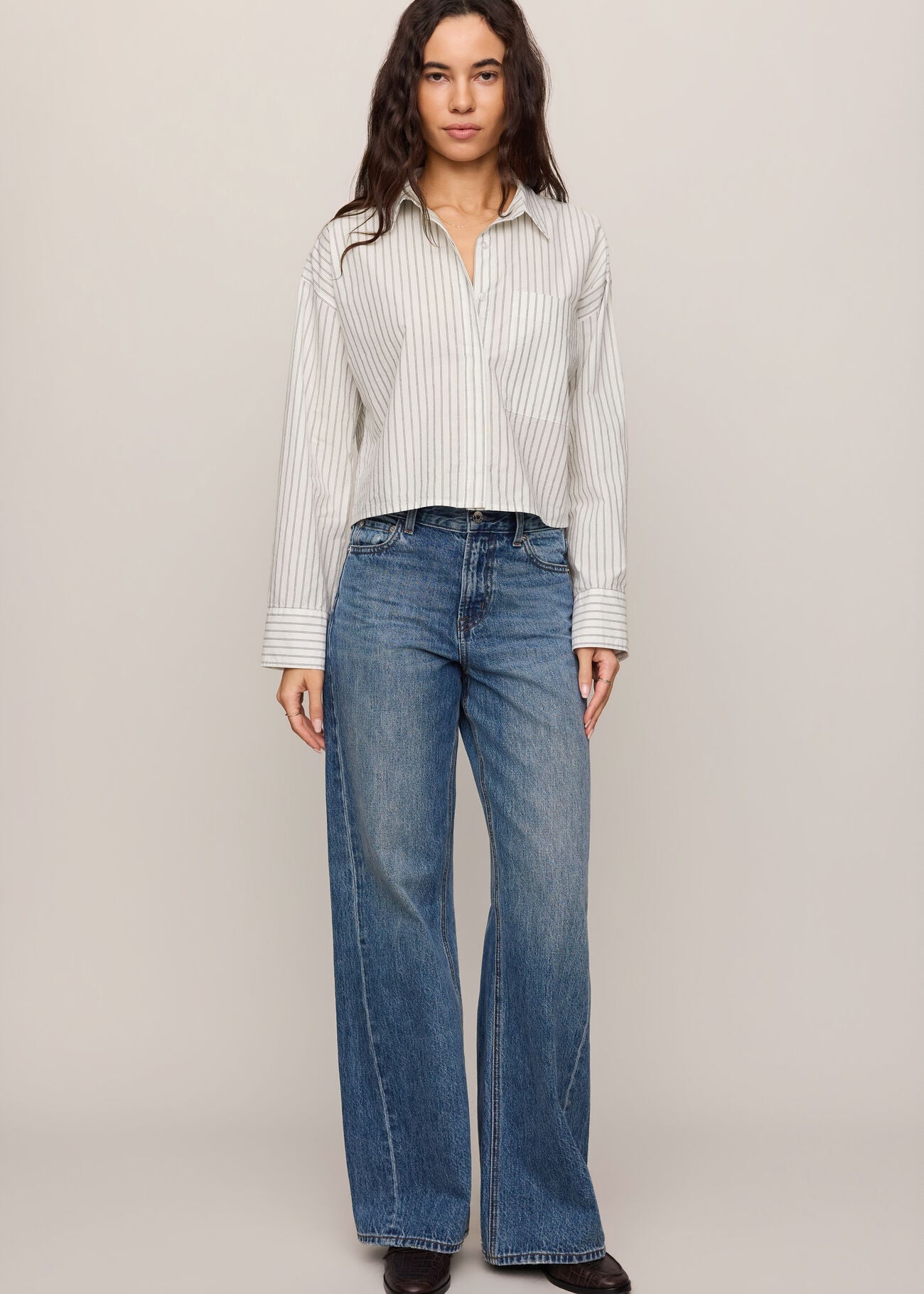 Woman wearing a striped shirt and blue jeans on a plain background