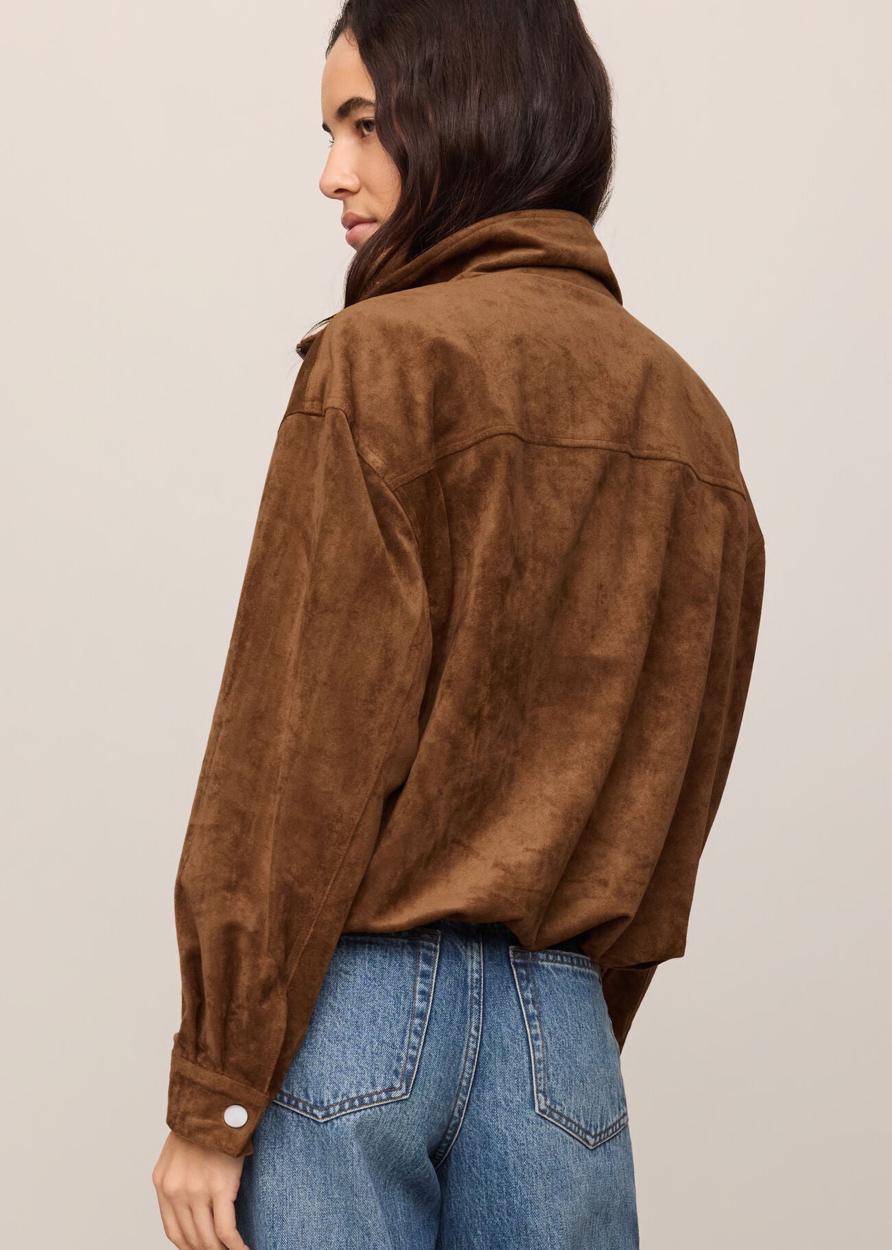 Person wearing a brown suede jacket and blue jeans on a plain background