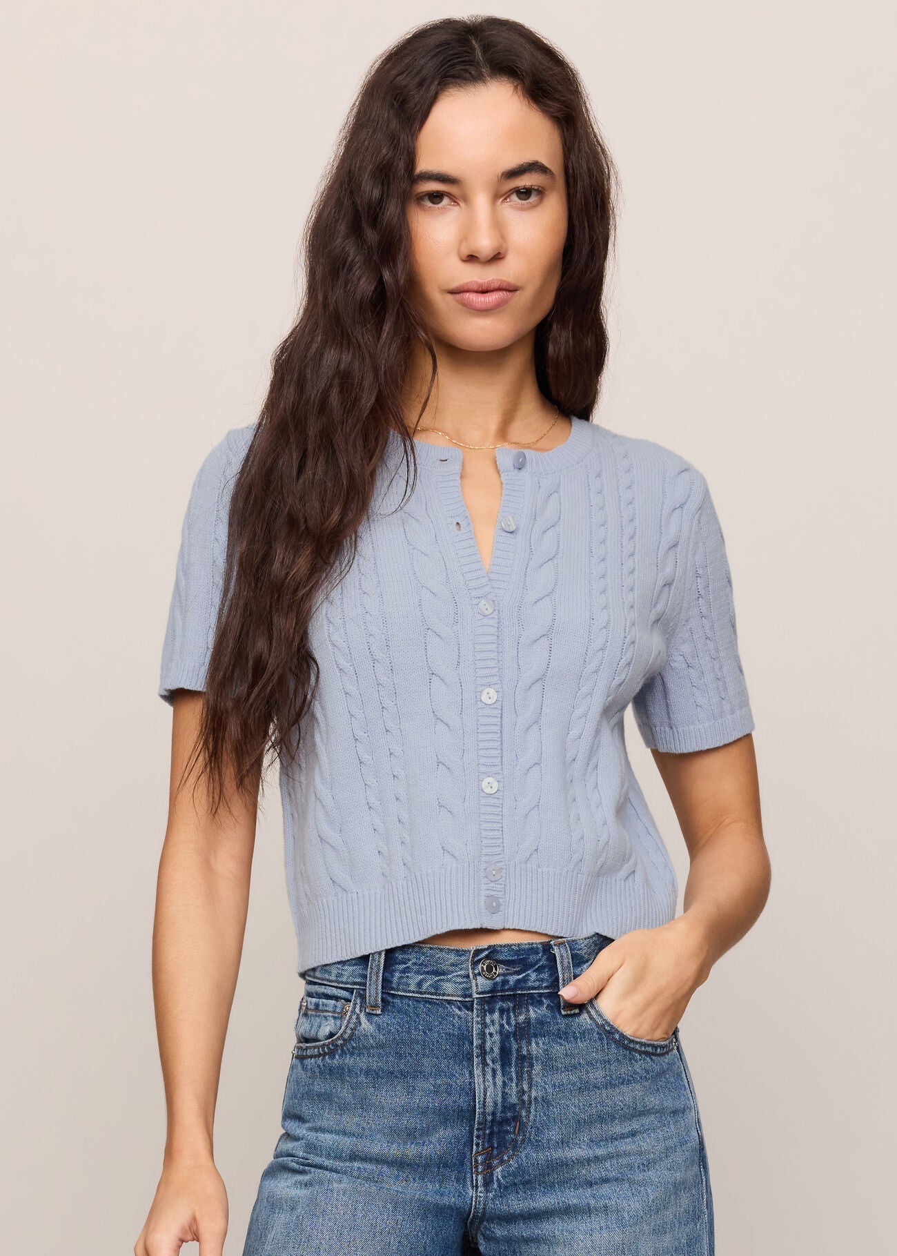 Woman wearing a light blue cable knit top and jeans on a beige background